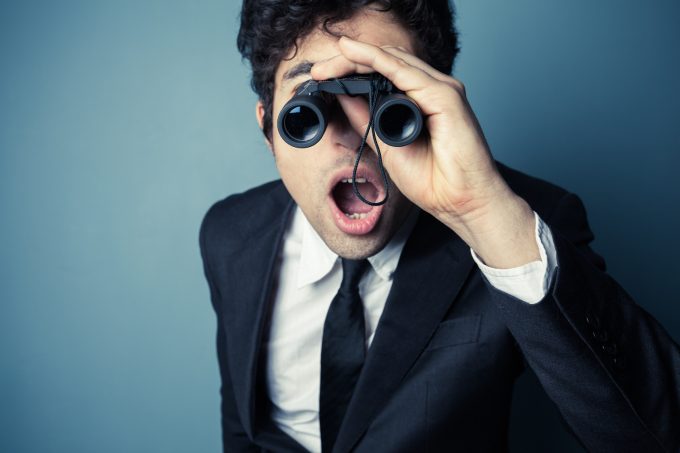 Young businessman is looking through binoculars and is surprised at what he sees