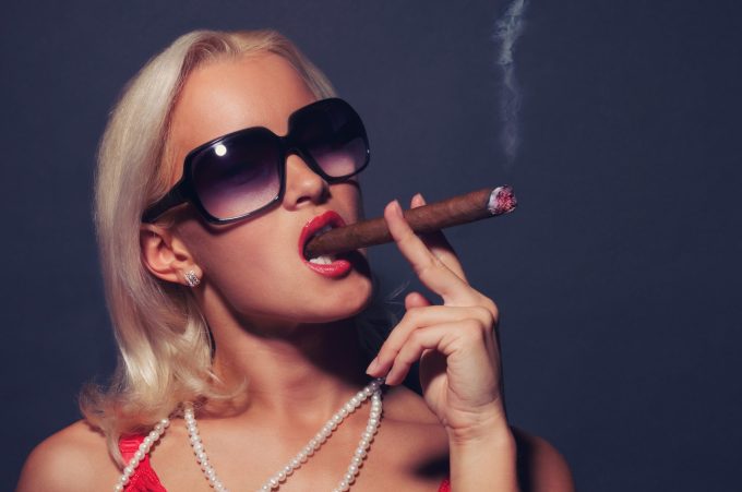 Blond woman in suglasses smoking cigar. Isolated on grey