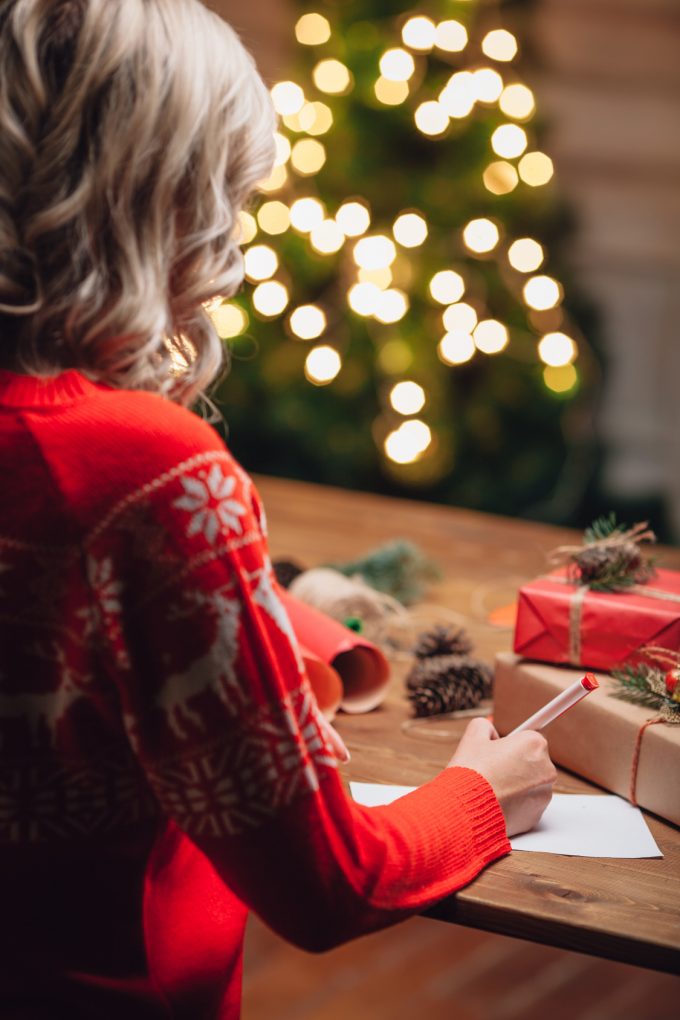 blonde woman writing on christmas postcard