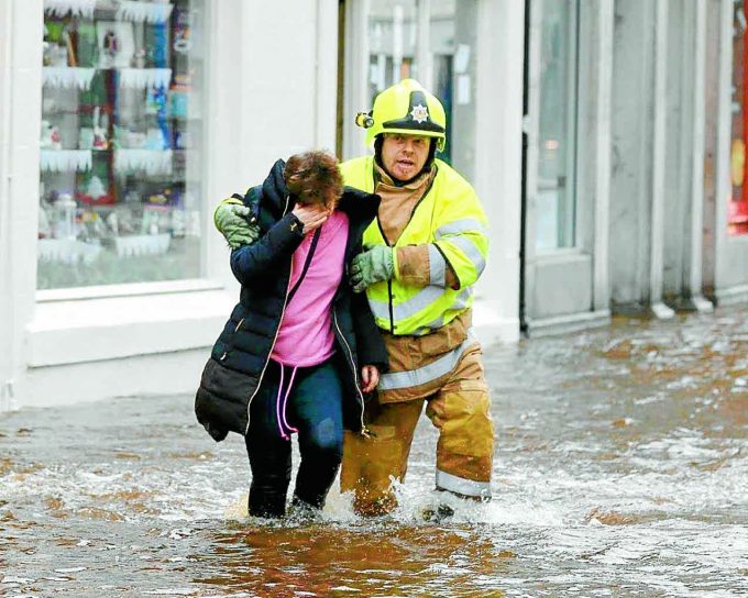 RESCUED . . . a firefighter helps a resident to safety during yesterday's flooding at Newton Stewart *** Local Caption *** RESCUED . . . a firefighter helps a resident to safety at Newton Stewart