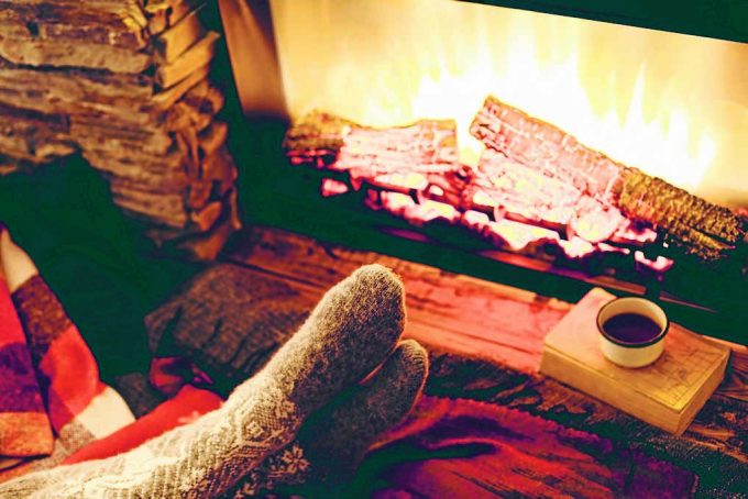 Cold fall or winter evening. People resting by the fire with blanket and tea. Closeup photo of feet in woolen socks. Cozy scene.